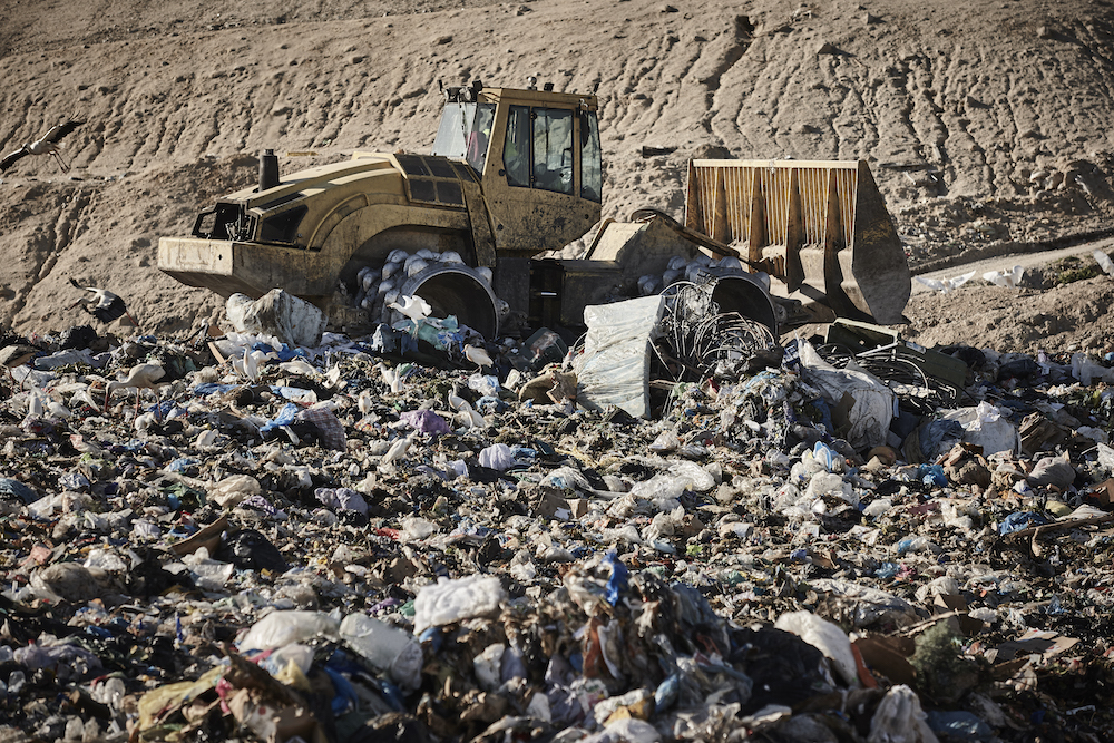 Heavy machinery shredding garbage in an open air landfill. Pollution